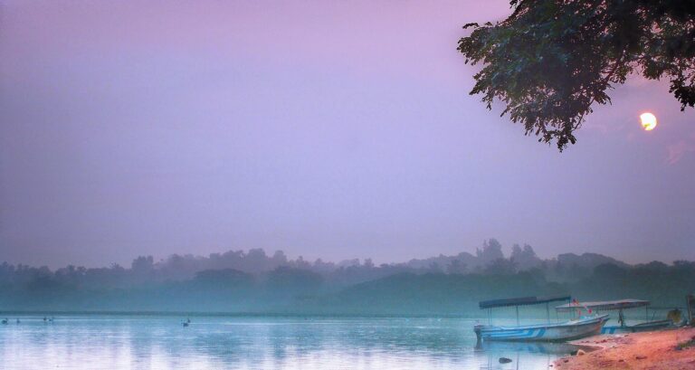 Misty sunrise over Ousteri lake near Pondicherry with tourist boats moored on the shore